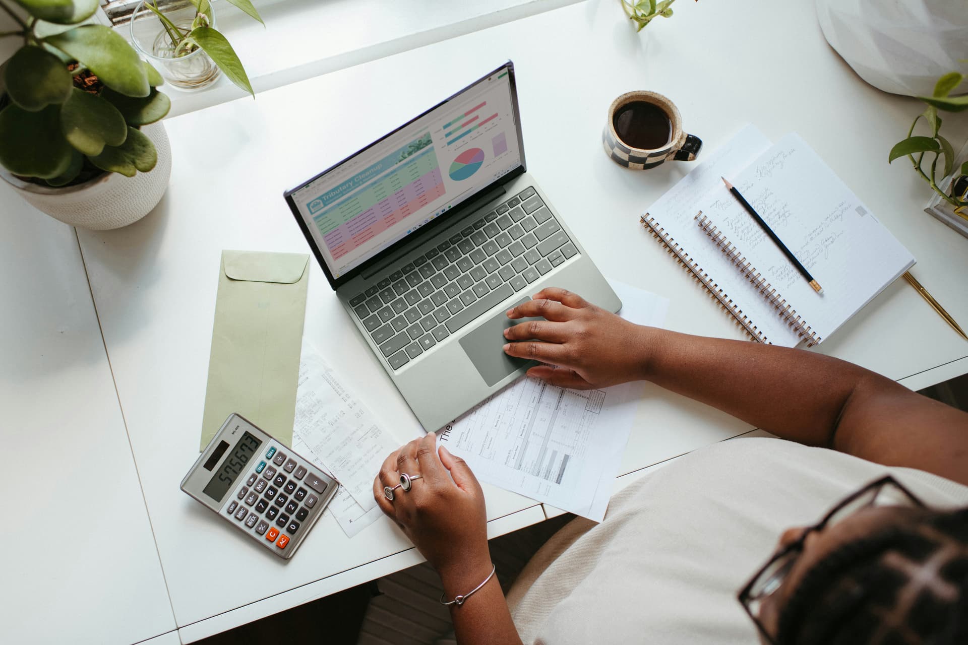 Accountant reviewing financial charts and invoices on a laptop with a calculator on the desk